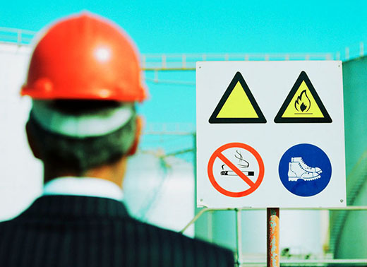 Businessman Wearing a Hard-Hat Looking at a Hazard Sign --- Image by © Royalty-Free/Corbis